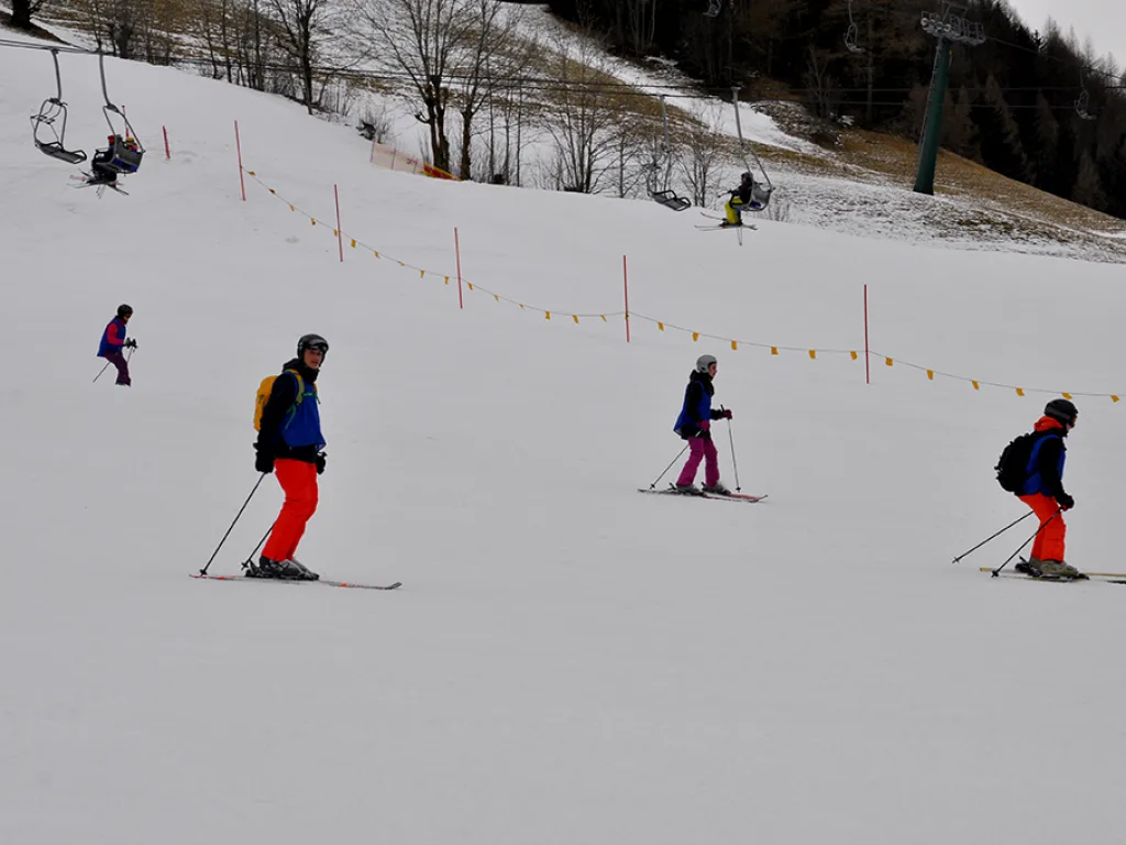 Drei Skifahrende an einer Absperrung entlang der Piste.
